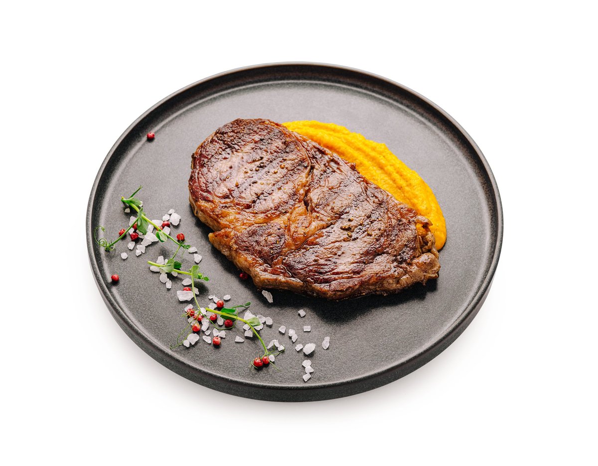 A cooked steak served with a side of mashed sweet potatoes